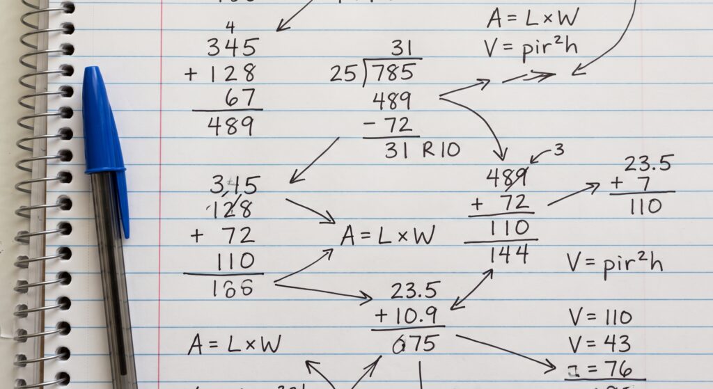 A close-up photograph of a page from a spiral-bound lined notebook filled with handwritten mathematical calculations and equations. Various long addition columns, long division steps, area (A=L*W), and volume (V=pir^2h) formulas are present. Arrows connect different numbers and formulas, creating a flow chart of a mathematical process. A blue ballpoint pen rests on the left side of the page, outside the red margin line.